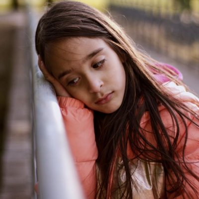 Anxious-looking young girl leaning her head against a metal fence railing 